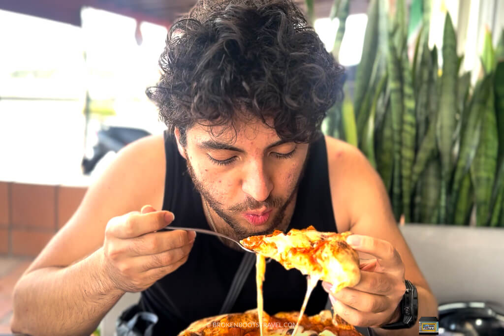 A man in a black tank top eating pizza in Guatapé, Antioquia